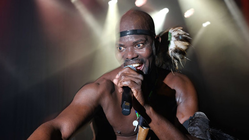 Musician Otim Alpha singing on stage under house lights.